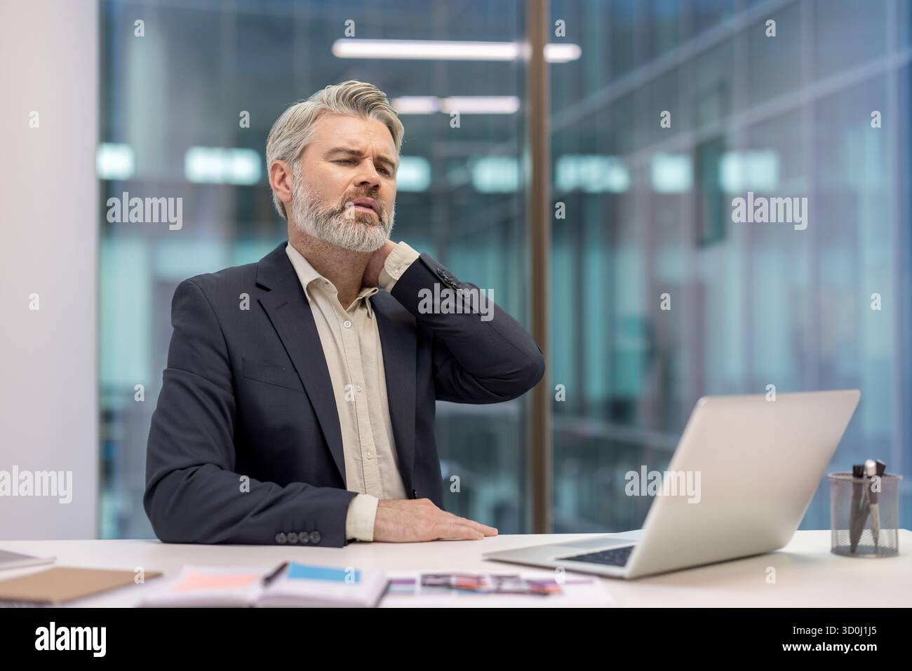Mature businessman sitting at his office desk with a laptop, looking ...