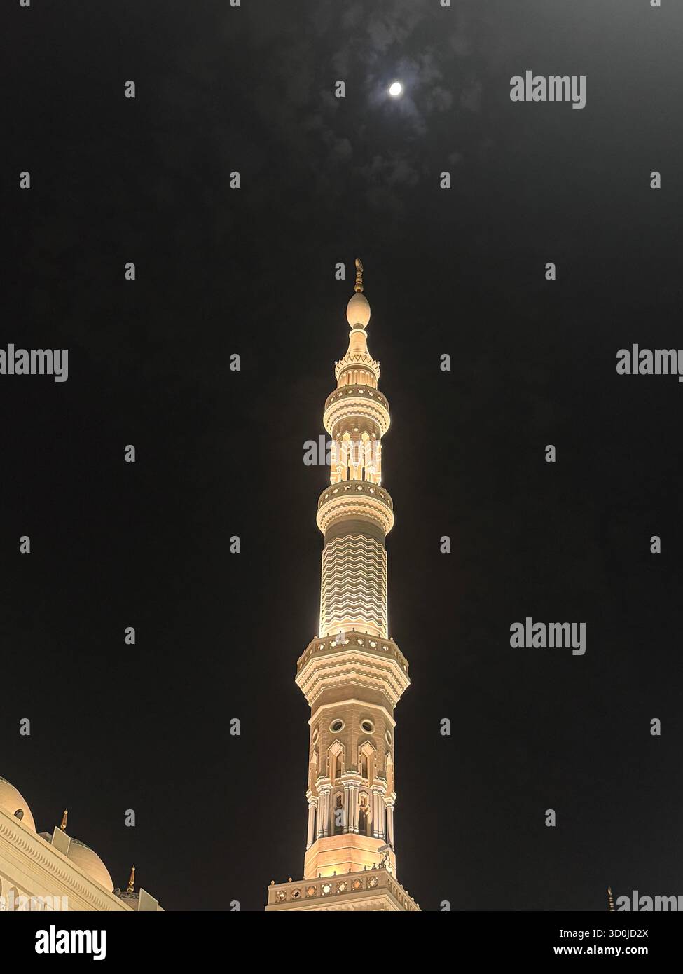 'Under the watchful eye of the moon, a beacon of light pierces the night sky. The minaret stands tall and luminous, a testament to faith and beauty. - Smartphone Captured Stock Image