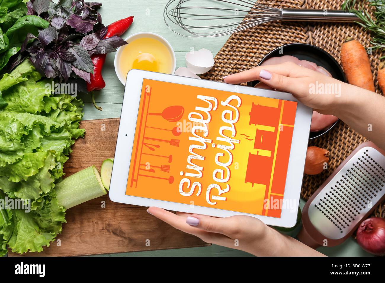 Hands holding tablet computer with recipe book on screen and products, top view Stock Photo