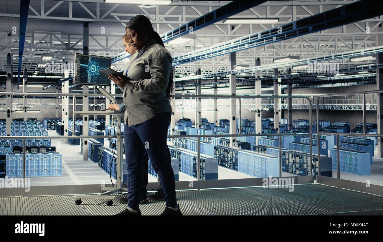 Data center software developers deploy machine learning software on infrastructure racks. Server room IT specialists train AI systems with datasets using tablet to support applications, camera A Stock Photo