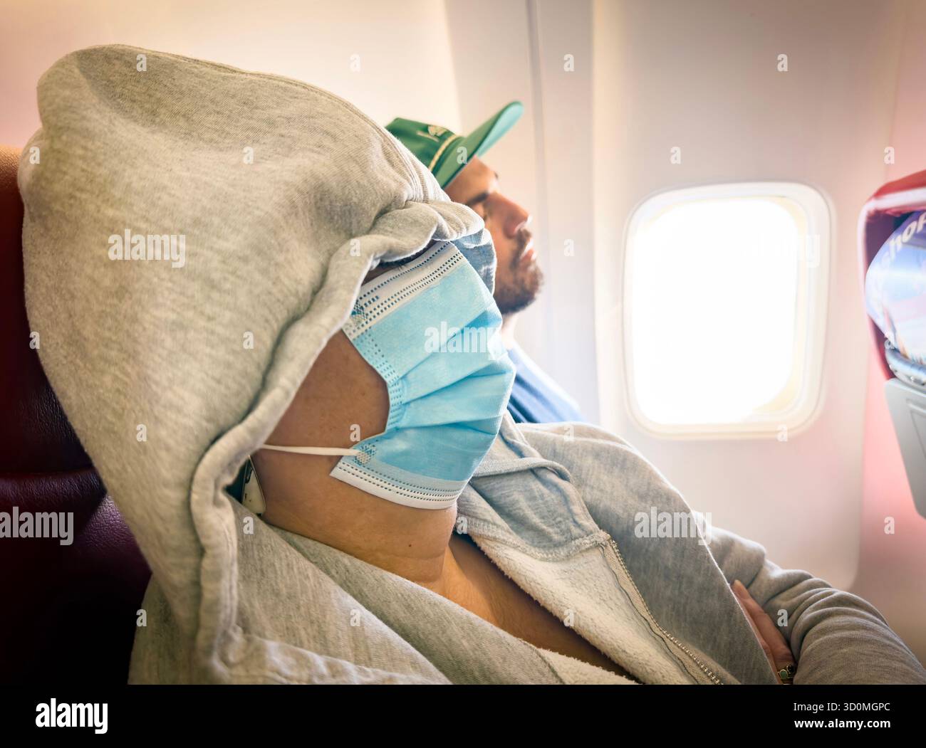 woman airline Passenger wearing face mask and hoodie sleeping during a commercial flight with sunlight coming through the airplane window - Smartphone Captured Stock Image