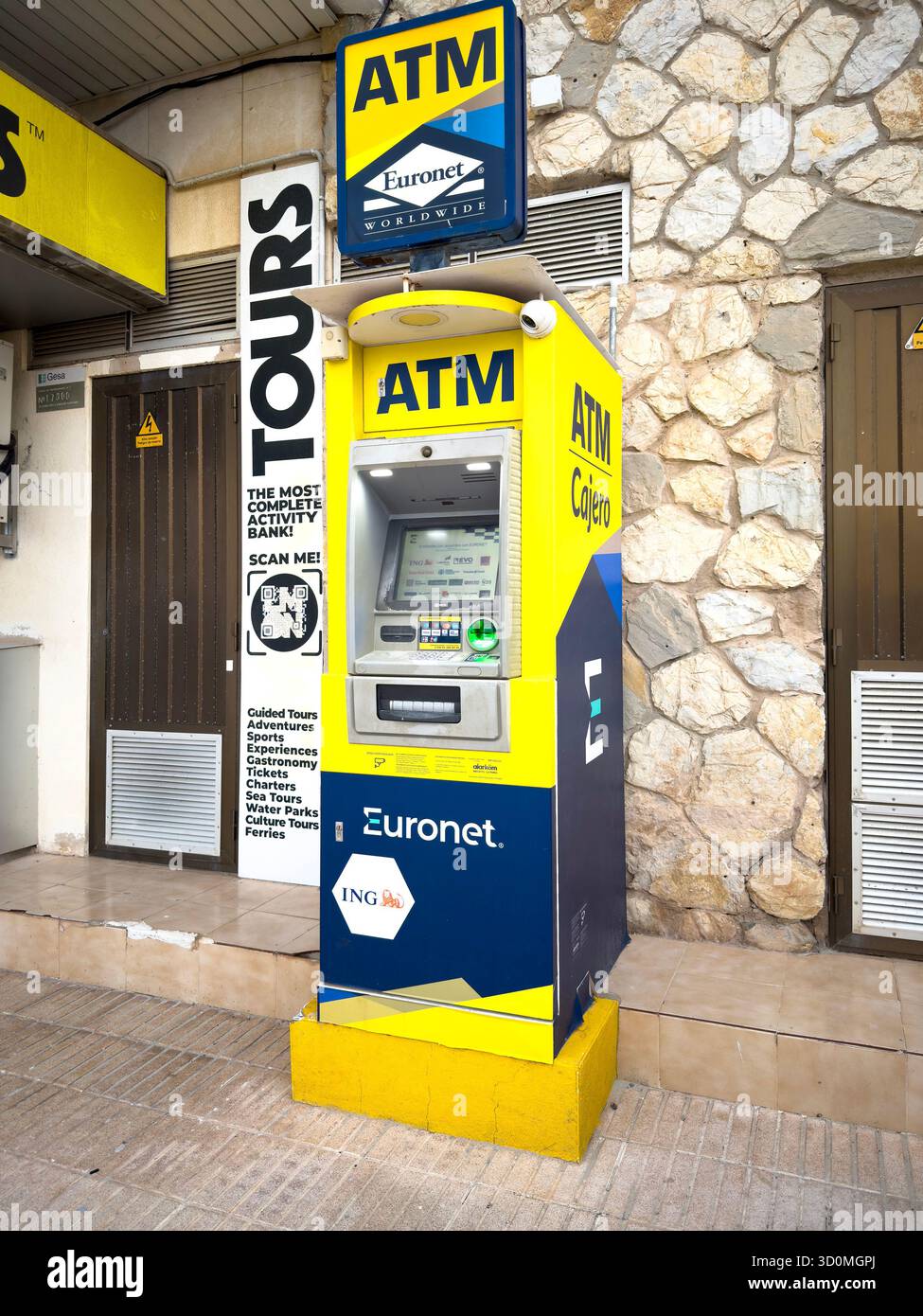 Outdoor Euronet ATM machine installed on a sidewalk next to a stone wall and tour office in a public urban area mallorca spain - Smartphone Captured Stock Image
