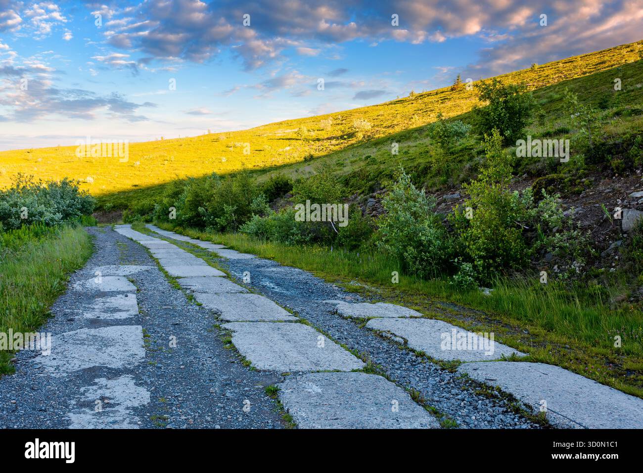 concrete road through carpathian mountains in morning light. cracked pavement of old military path near the steep green hill. summer landscape of ukra Stock Photo