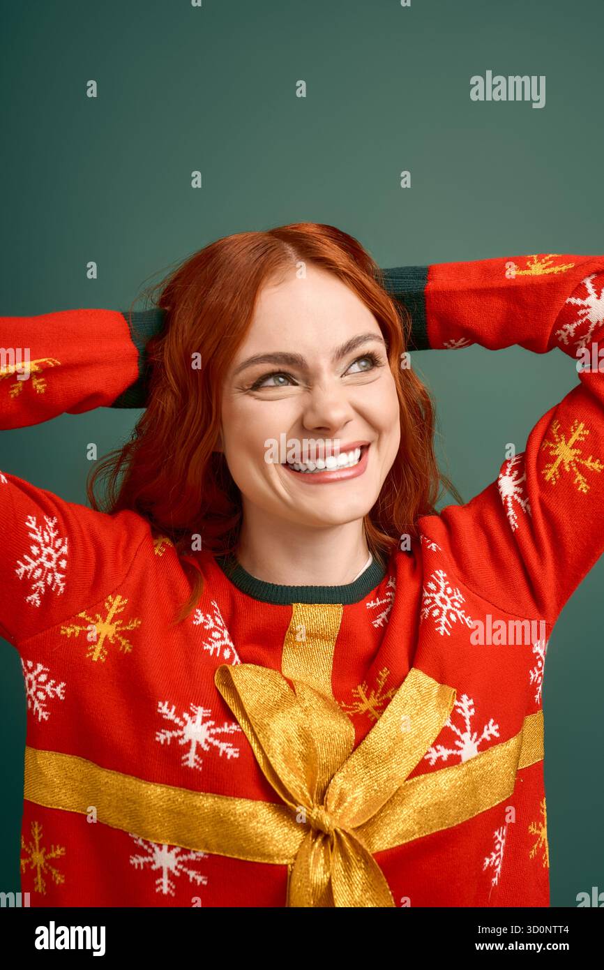 A red-haired woman showcases her cheerful personality in a Christmas sweater on a green backdrop. Stock Photo