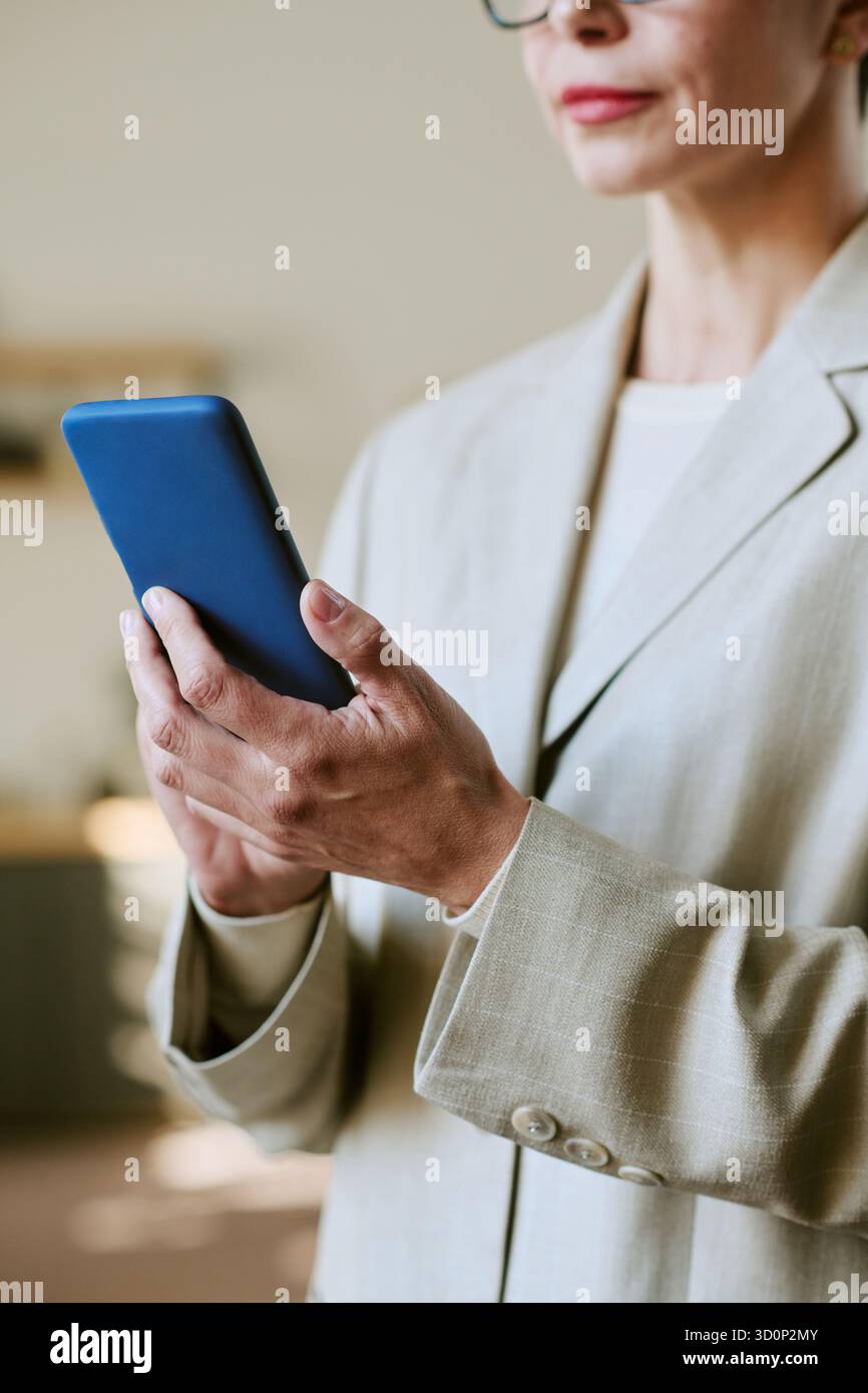 Middle Aged Woman Using Smartphone While Standing Indoors Stock Photo