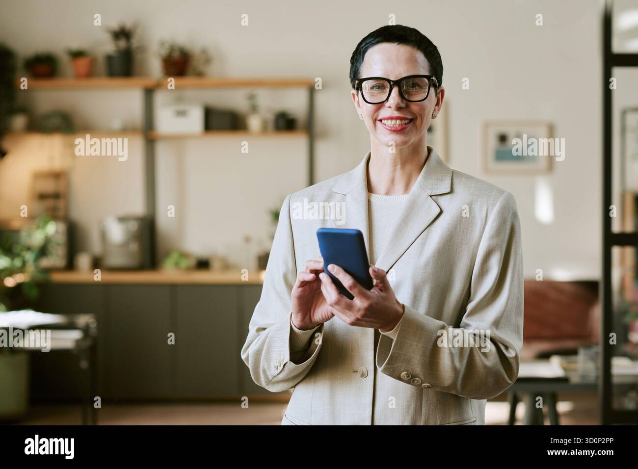 Portrait of Middle Aged Woman Smiling While Using Smartphone Indoors Stock Photo