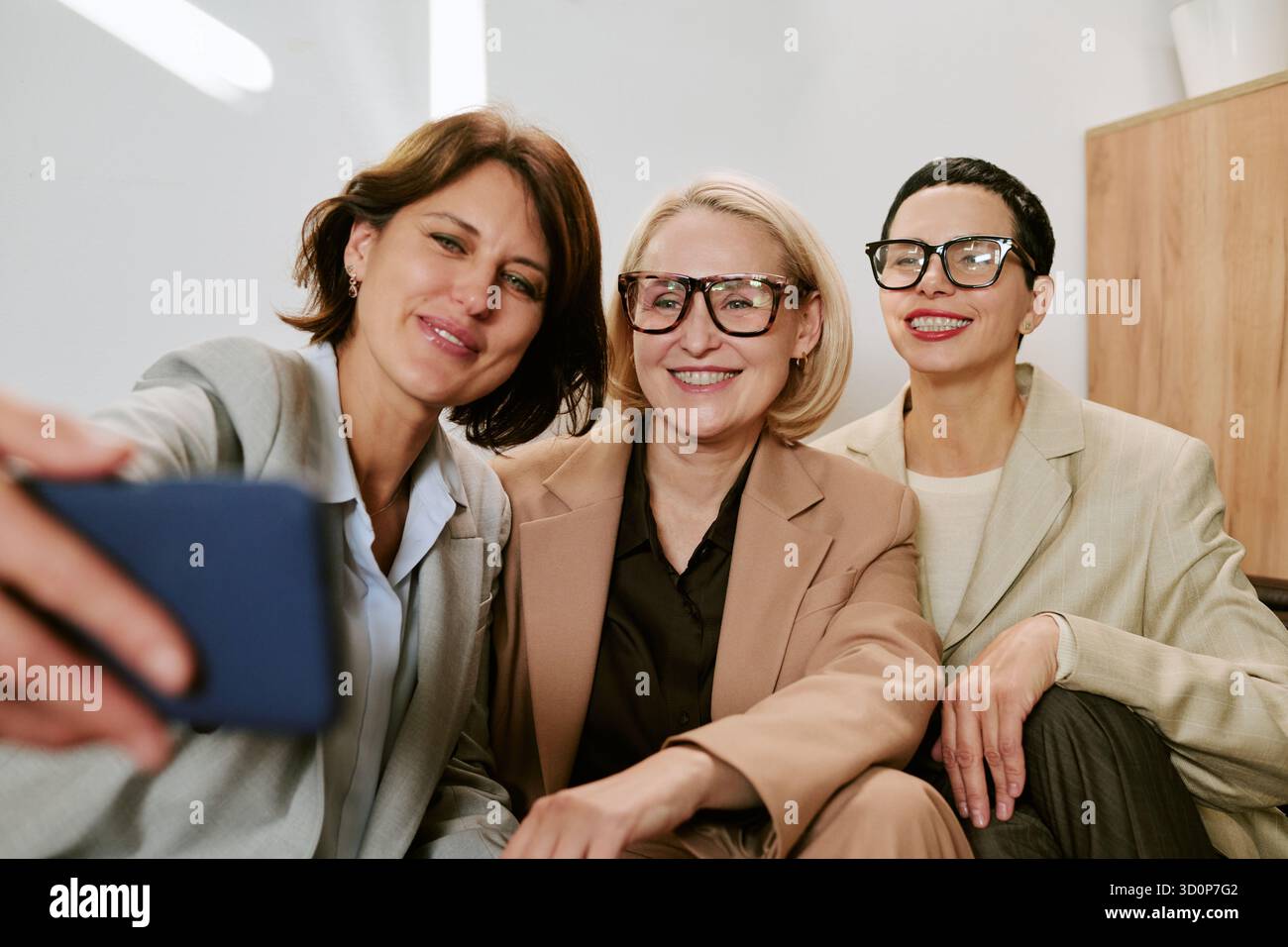 Three Middle Aged Women Smiling While Taking Selfie Indoors Stock Photo