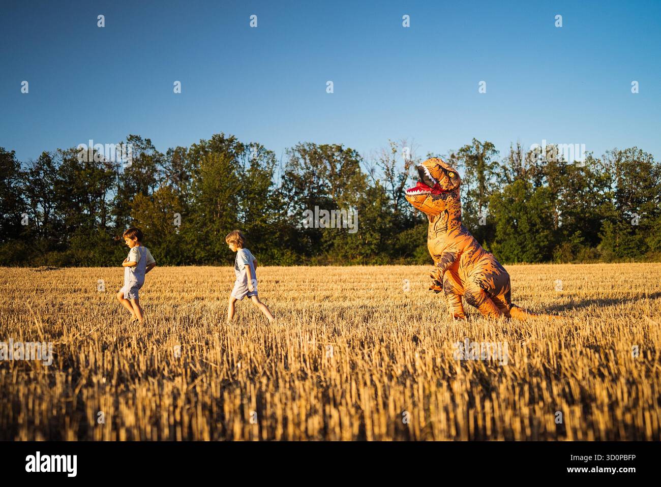 Funny scene of children running across dry meadow while person dressed ...