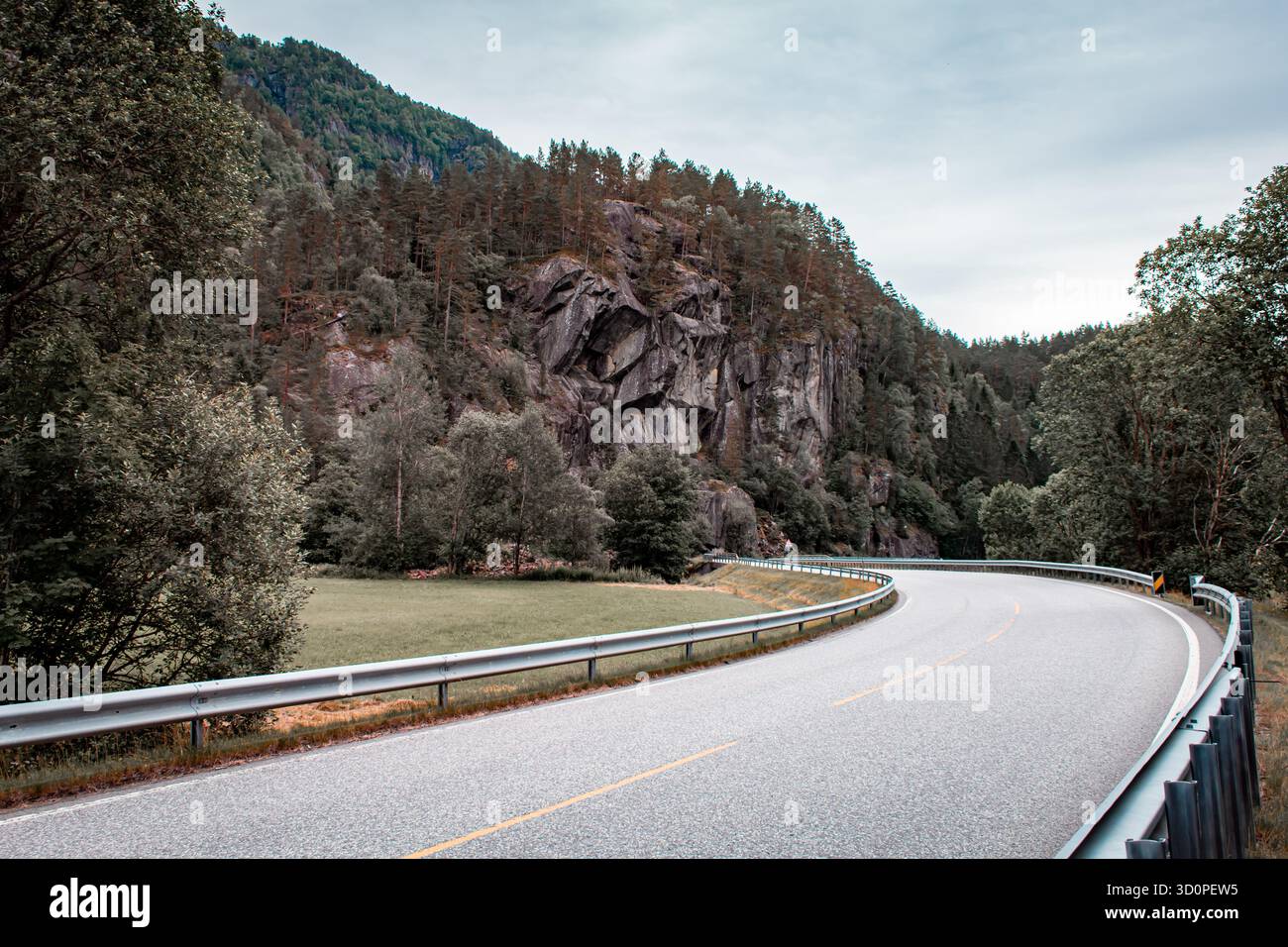 A paved road along which there are cliffs covered with forest. Stock Photo