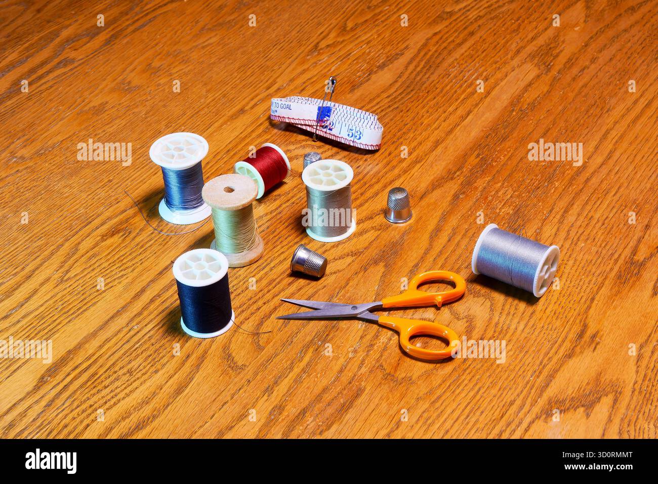 Spools of colored thread, thimbles, scissors and a tape measure on a wooden surface. Stock Photo