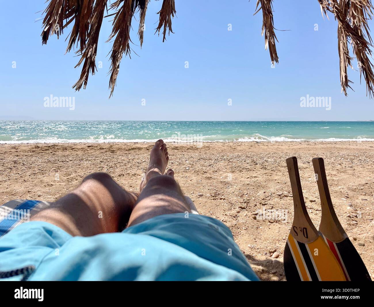 A man lying on the beach under palm trees and beach racket, Red Sea, Egypt - Smartphone Captured Stock Image