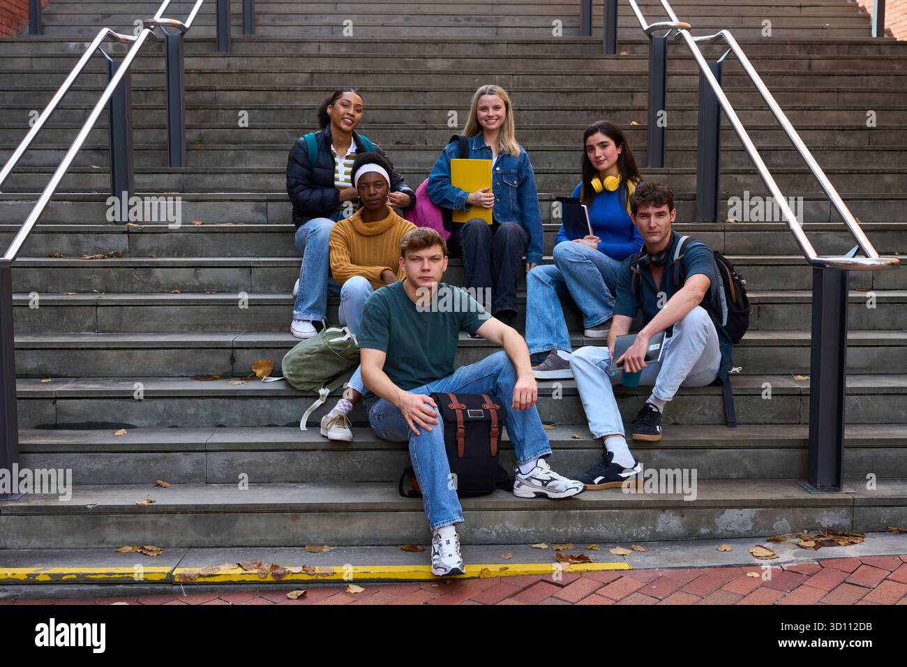 Diverse students sitting on campus stairs looking at camera Stock Photo