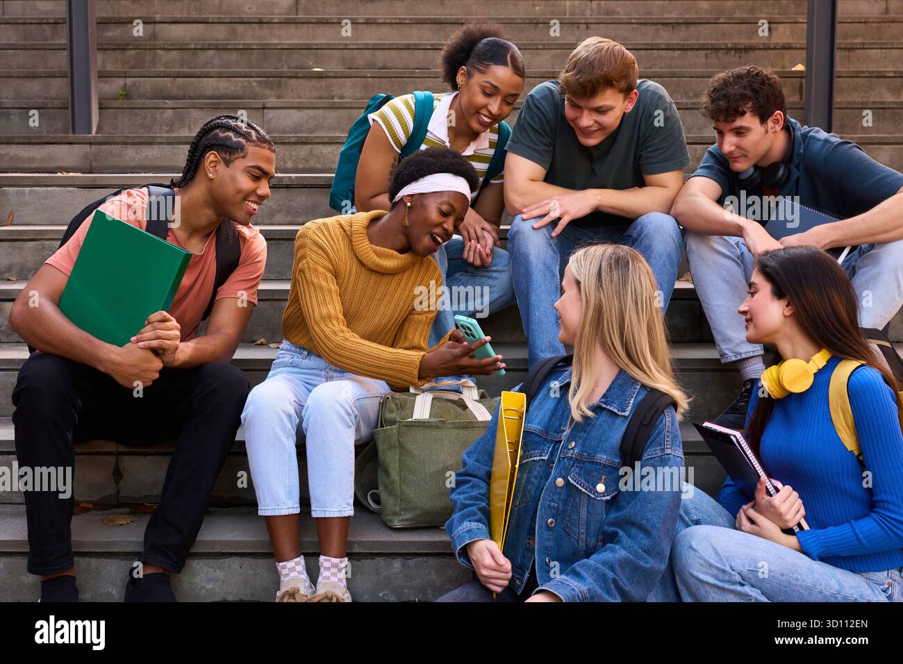 Diverse student group interacting, sharing smartphone on stairs Stock Photo