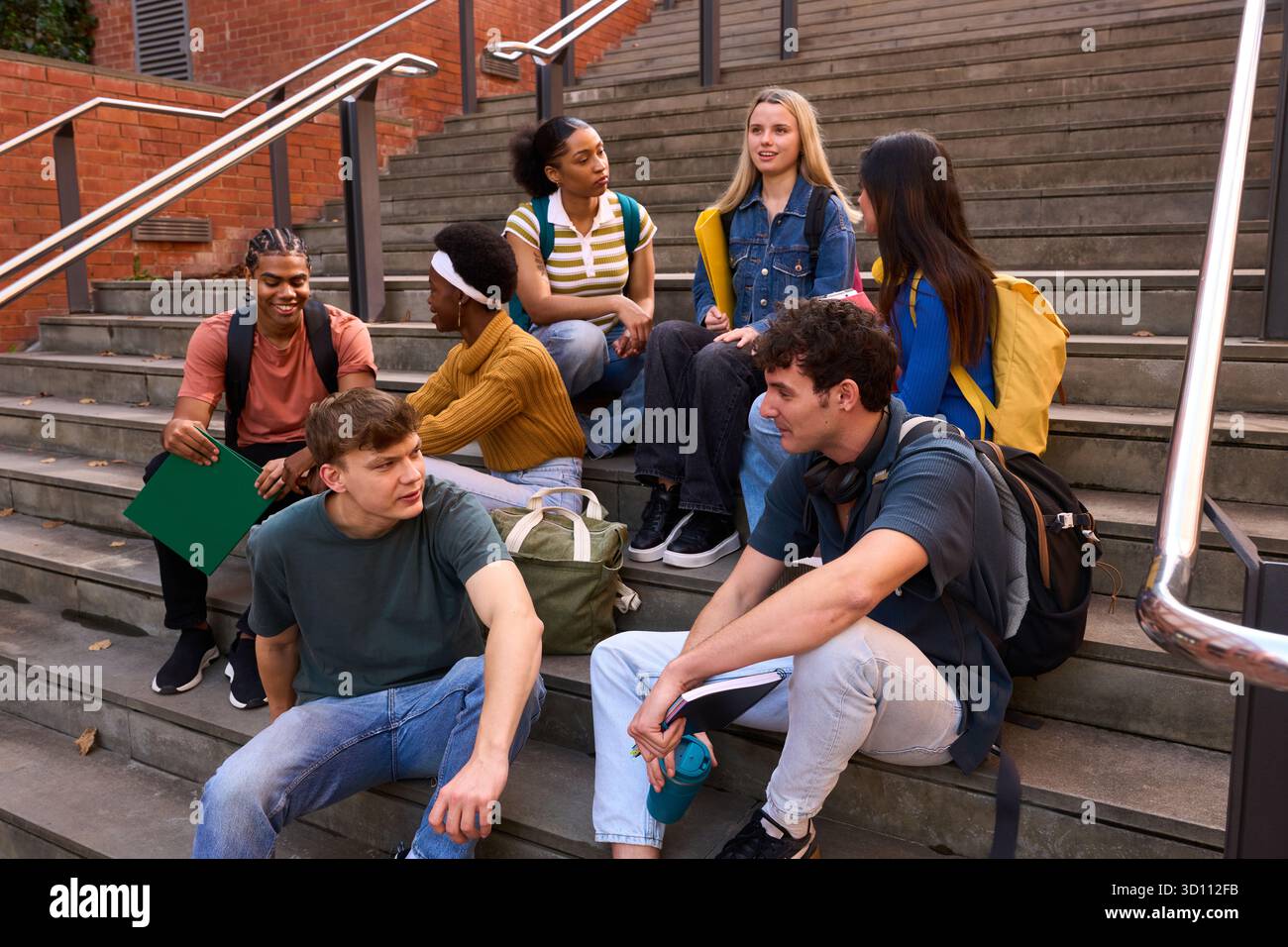 Diverse young adults studying talking on campus stairs Stock Photo