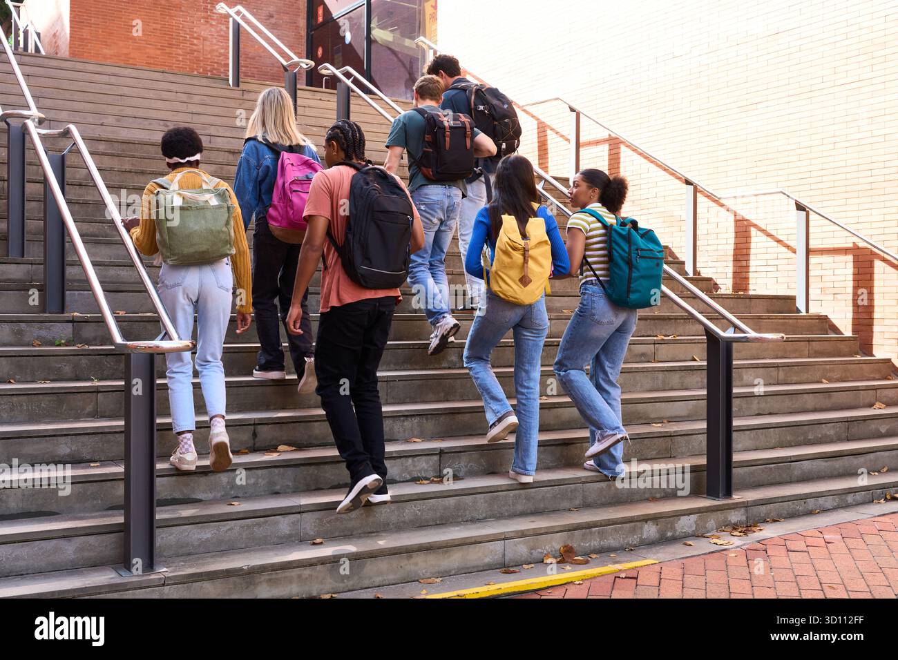 Diverse students walking up school stairs on campus Stock Photo