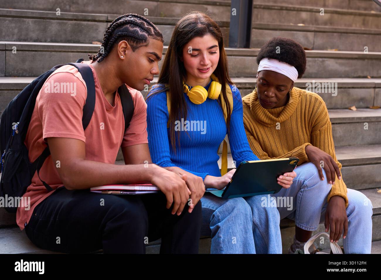 Diverse students collaborating on tablet at university stairs Stock Photo