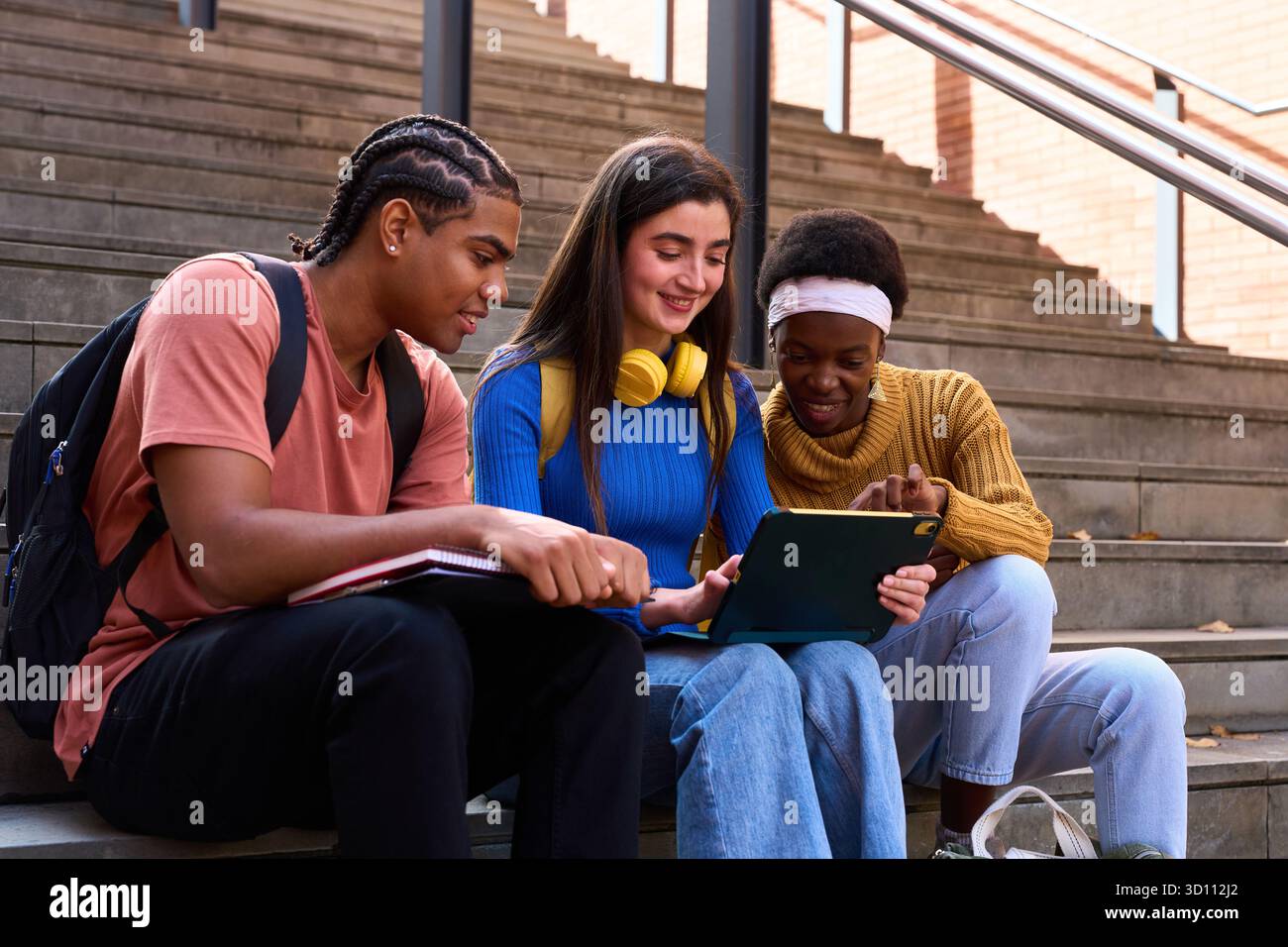 Diverse students learning together on tablet on campus stairs Stock Photo