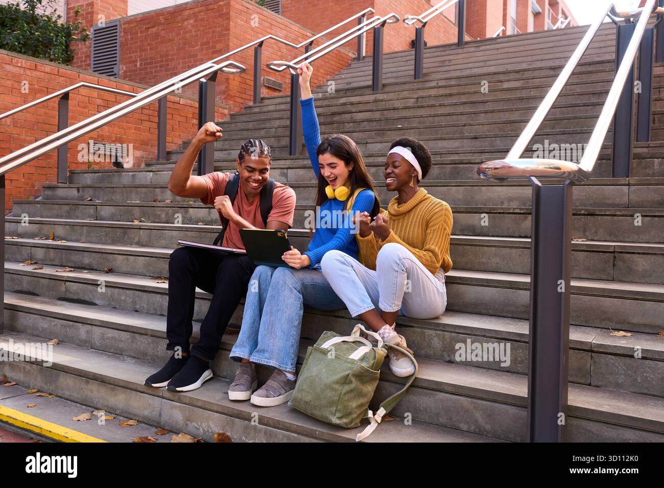 Diverse university students celebrating academic success on campus stairs Stock Photo