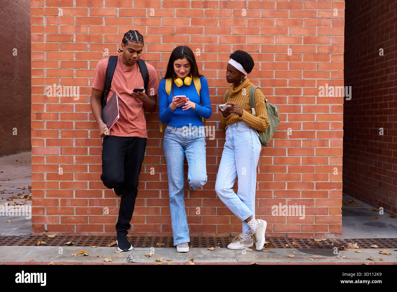 Diverse students using smart phones against brick wall Stock Photo