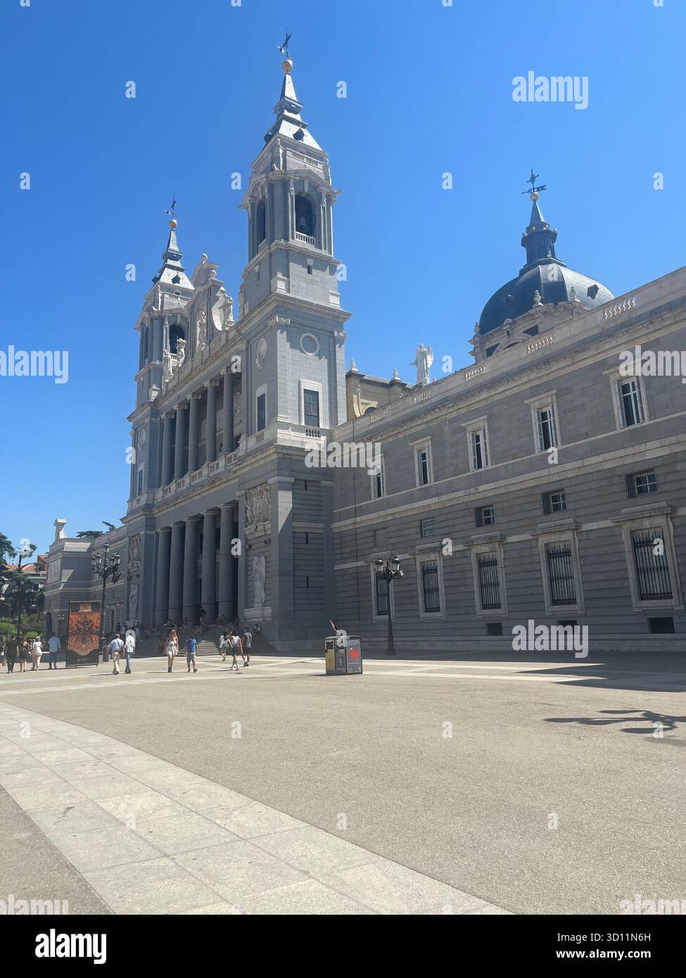 Side view of the Almudena Cathedral in Madrid, Spain, with its twin towers and part of the Plaza de la Armería on a sunny summer day. - Smartphone Captured Stock Image