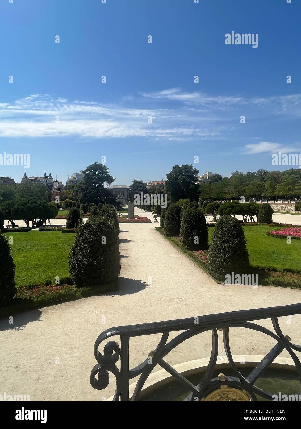 Sunny view of El Retiro Park in Madrid with manicured gardens, pathways, and lush greenery under a bright summer sky. - Smartphone Captured Stock Image