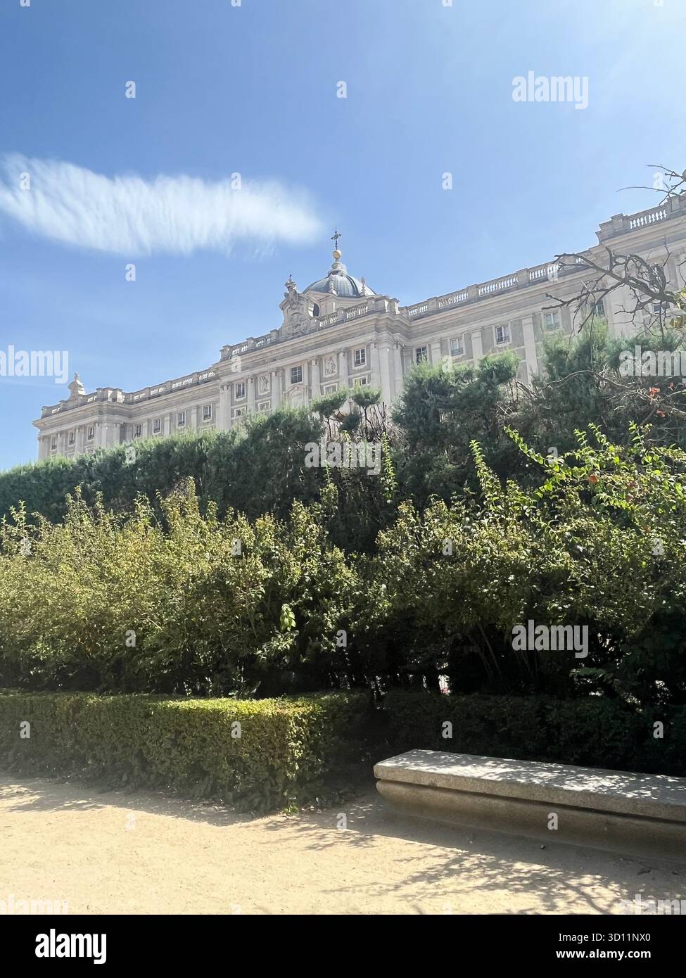Side View of the Royal Palace of Madrid from Jardines de Sabatini on a Sunny Summer Day with Blue Sky, Trees, Garden Bench and a Beautiful Cloud. - Smartphone Captured Stock Image