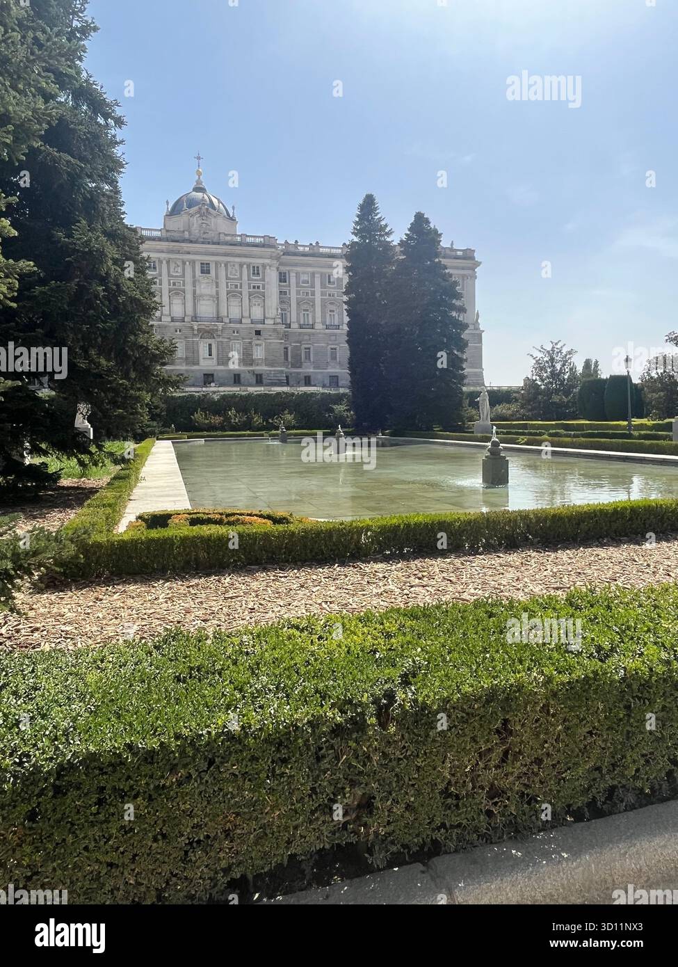 Royal Palace of Madrid Seen Above Garden Basin in Jardines de Sabatini with Trees, Bushes and a Bright Blue Summer Sky on a Sunny Day. - Smartphone Captured Stock Image