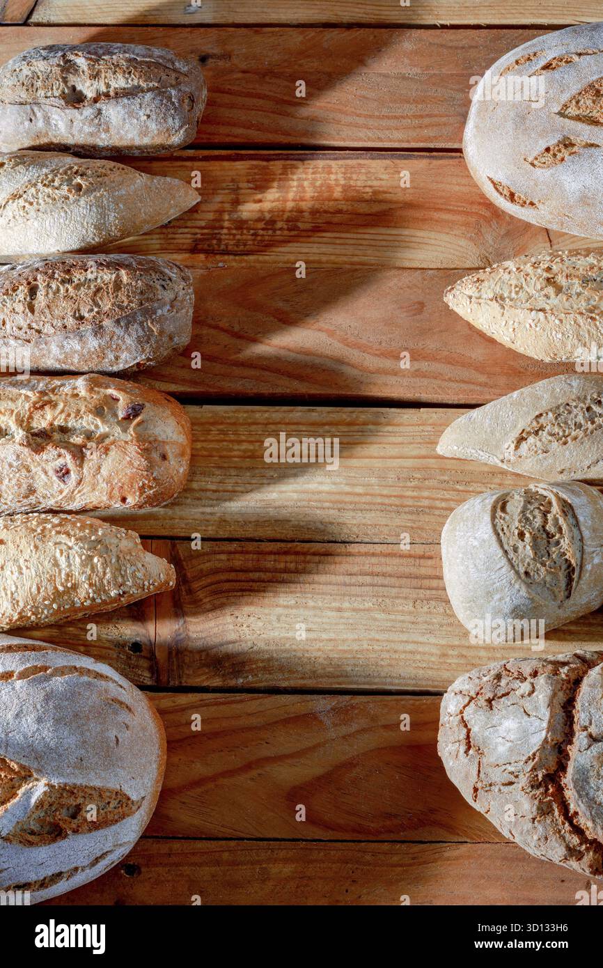 Various types of fresh artisanal bread, including baguettes and round loaves, arranged on a rustic wooden table Stock Photo