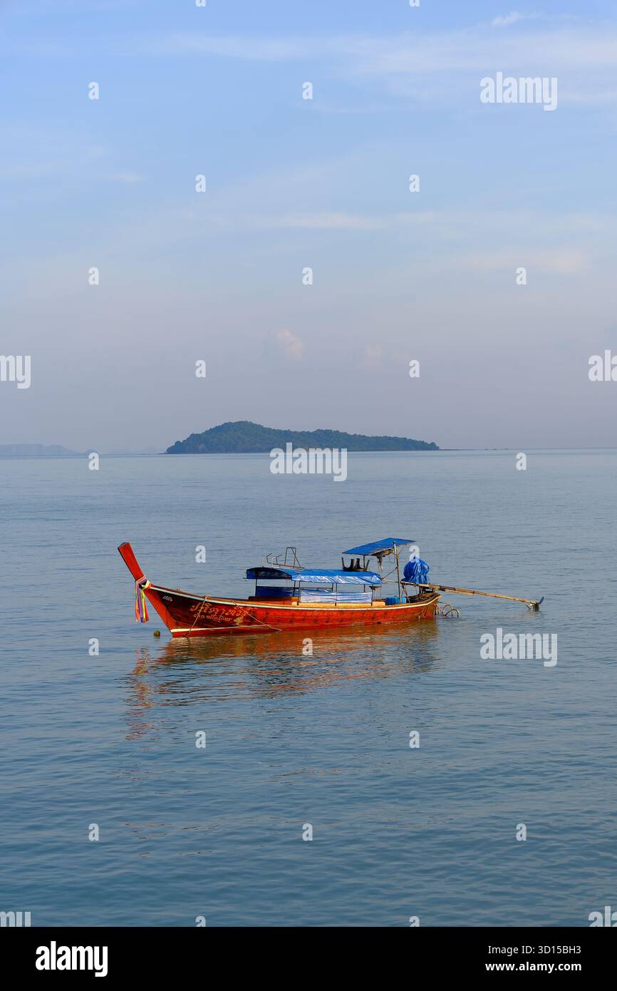 Traditional longtail boat floating on calm turquoise waters near Krabi, Thailand, with a distant island on the horizon. Stock Photo