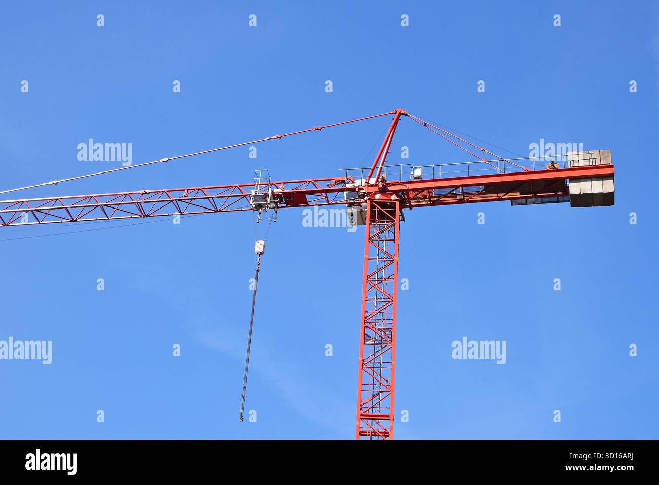Red tower crane superstructure extending across a clear blue sky ...