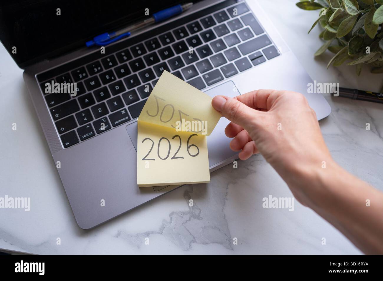 Hand changing a sticky note calendar from 2025 to 2026 on a laptop ...