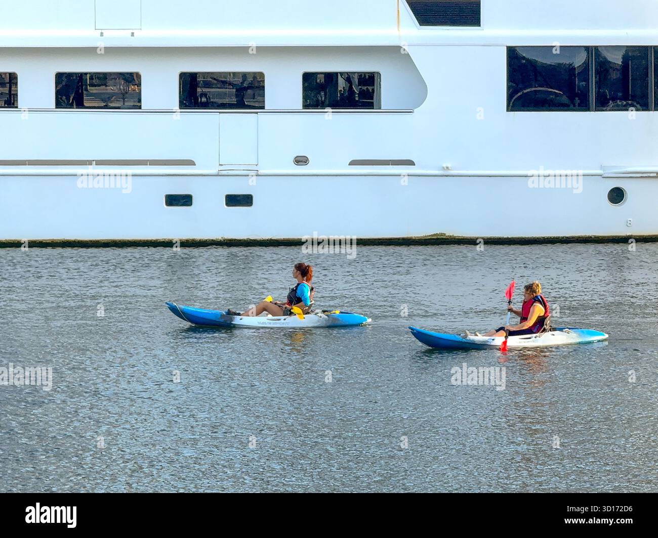 Bristol, Avon, England, UK - 25 April 2025: Paddle boarders sitting down and paddling alongside boats in the regenerated Bristol City Docks area. - Smartphone Captured Stock Image