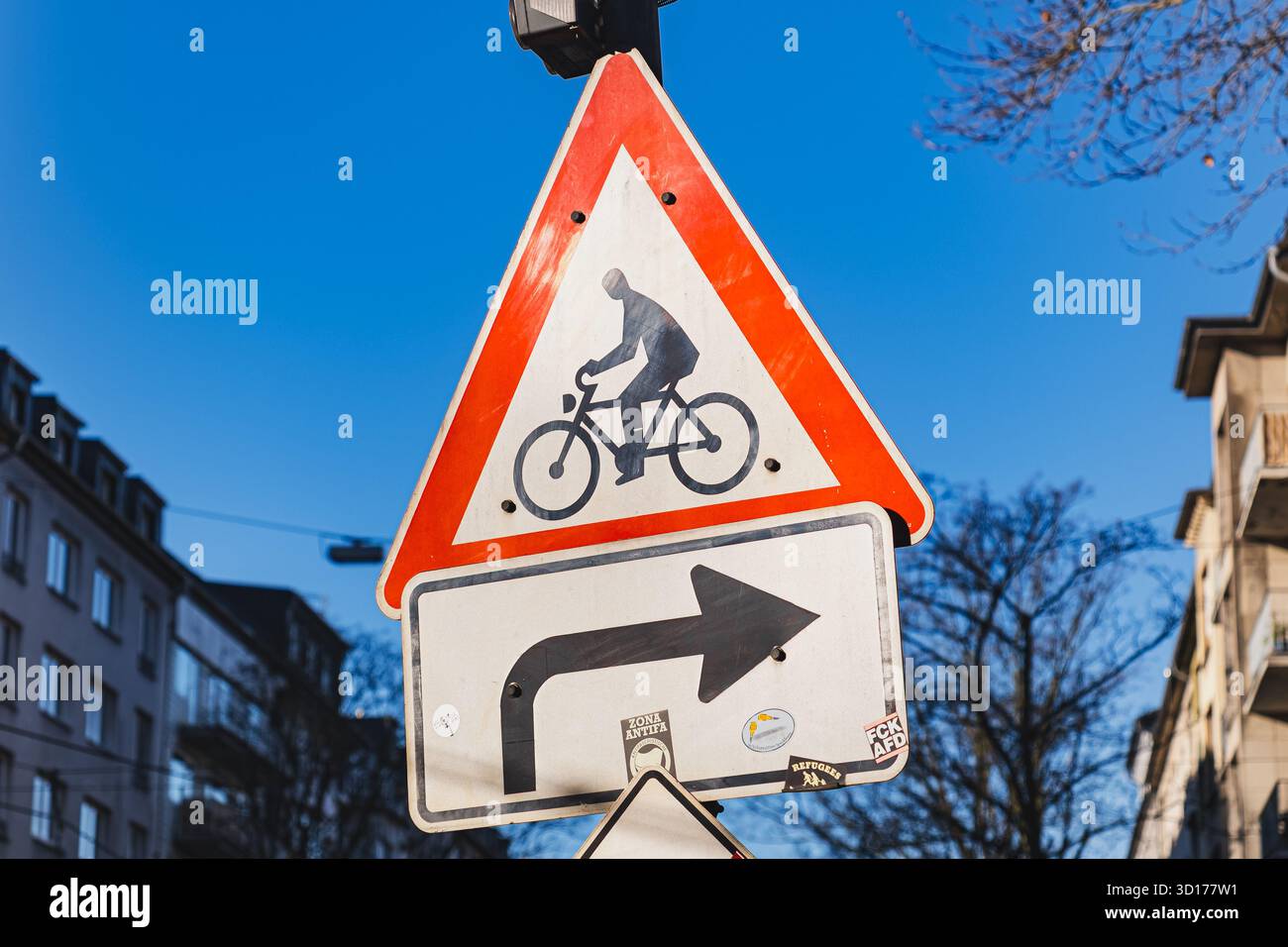 A bicycle warning sign with a right-turn arrow against a clear blue sky ...