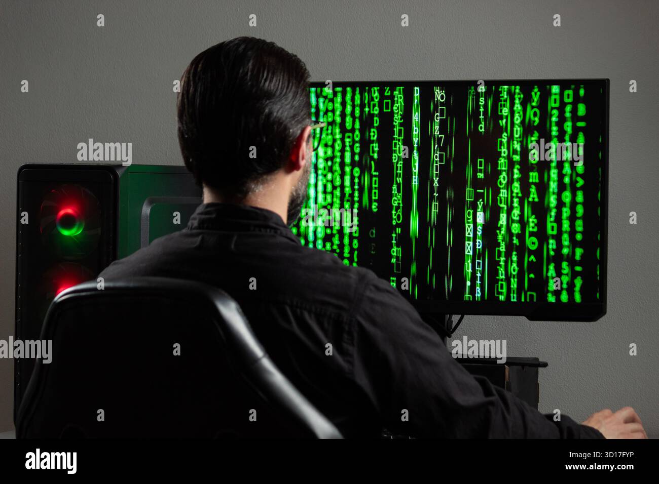 Close up to a man backward watching a computer monitor with a green matrix code on the screen Stock Photo