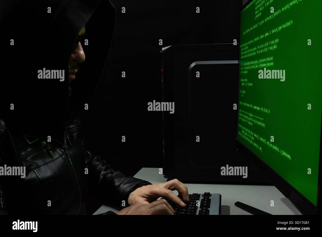 close up to a hooded hackerman writing a green html code into a computer keyboard Stock Photo