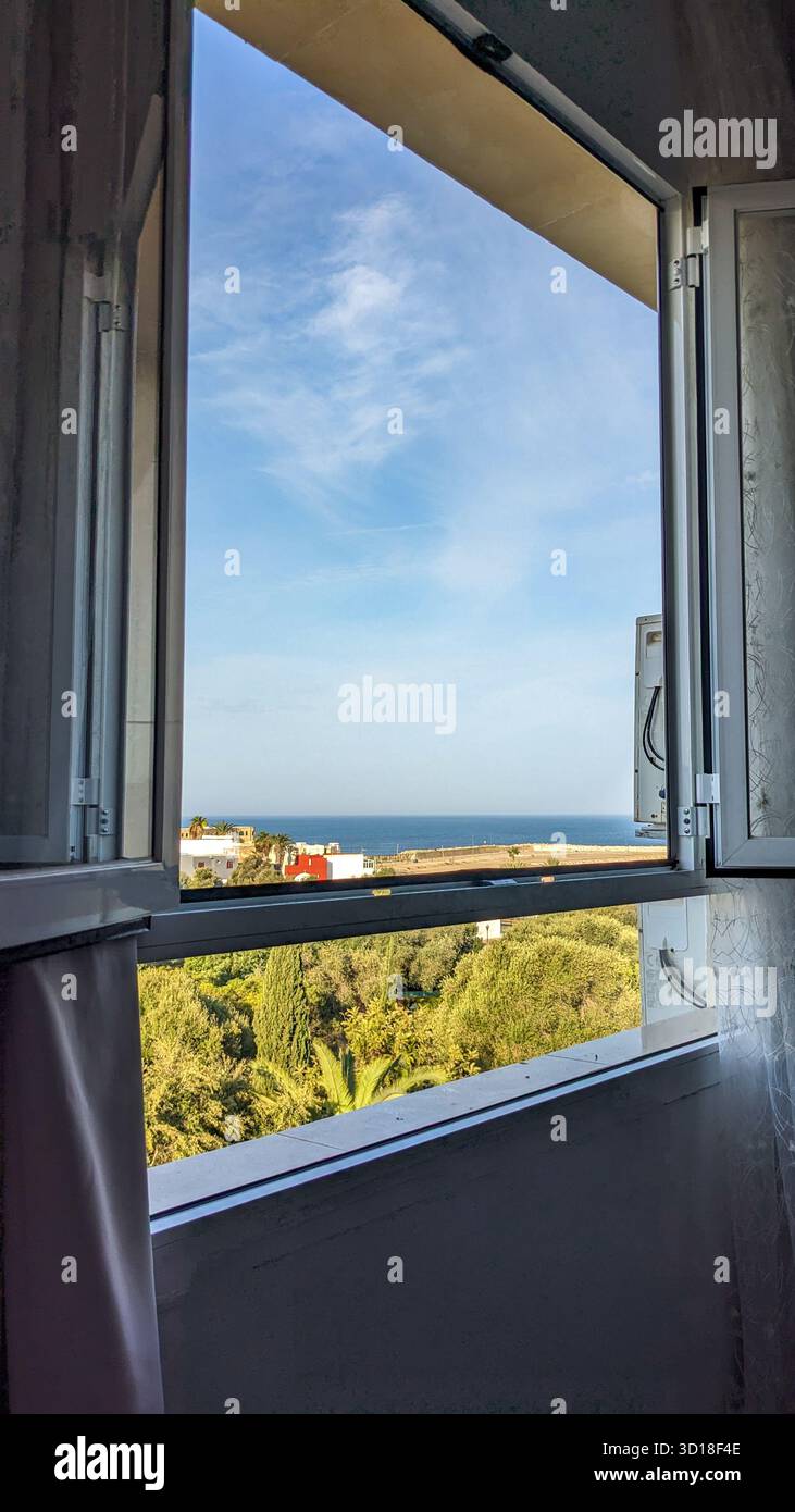 Bright view framed by an open window overlooking the blue Mediterranean sea and lush green coastal vegetation on a sunny day. vacation / travel - Smartphone Captured Stock Image