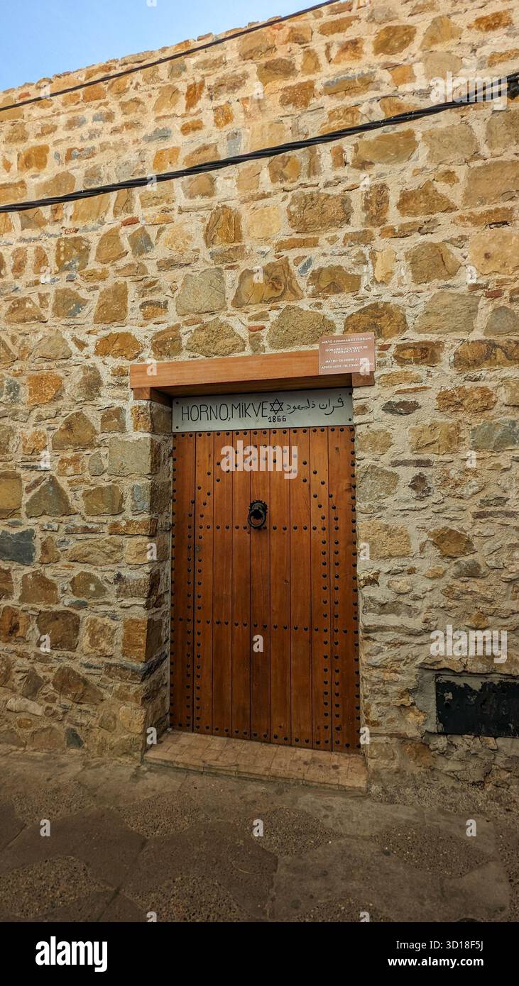 historic wooden door of a former jewish mikveh and community oven set in a rough stone wall with bilingual sign - Smartphone Captured Stock Image