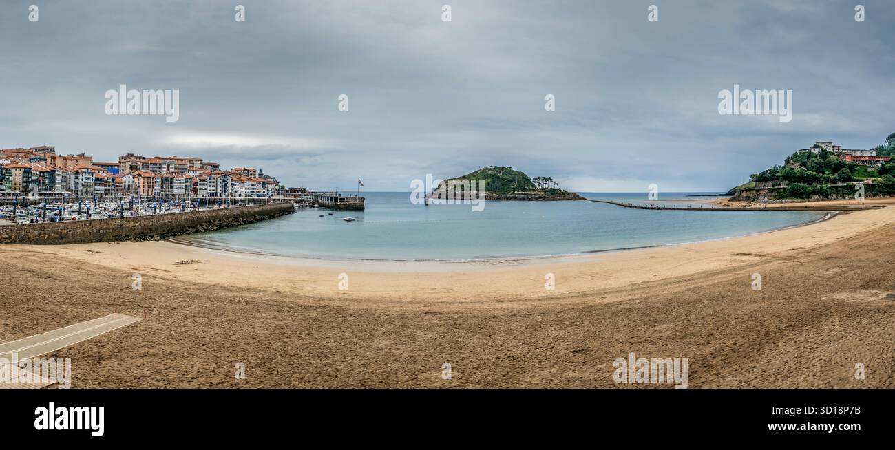 Panoramic view of Isuntza Beach in Lekeitio, with the historic fishing port, colorful town, and San Nicolas (Garraitz) Island, Bizkaia, Spain Stock Photo