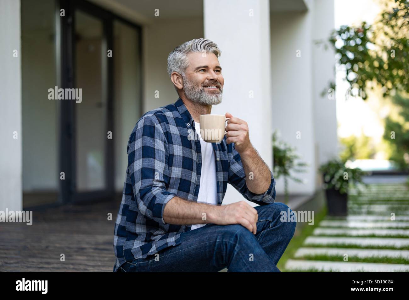 Gray-haired mature man sitting in his house yard and having morning coffee Stock Photo