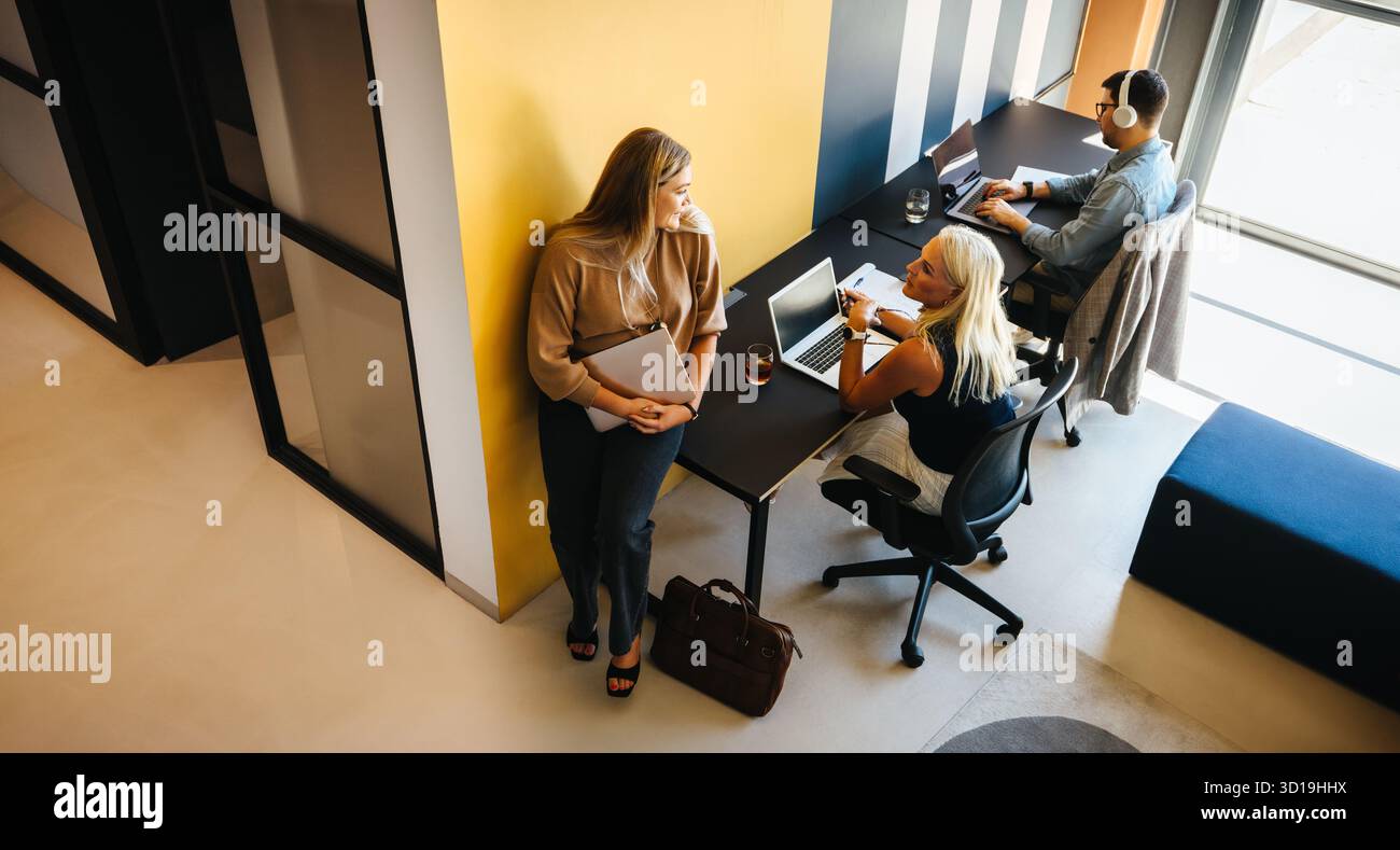 Three adults in a contemporary office setting, engaging in work activities using technology in a professional environment. Stock Photo