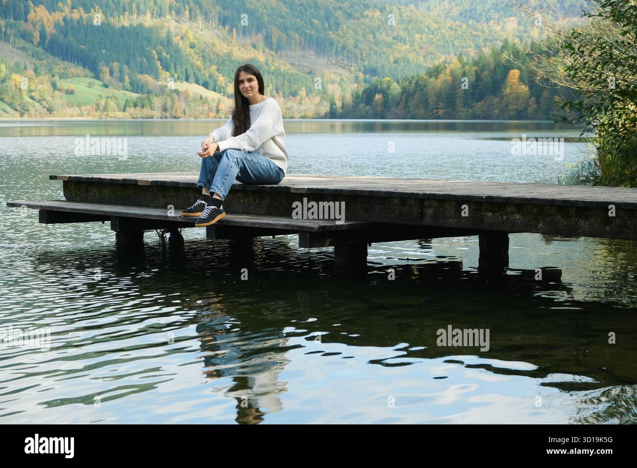 Brunette Woman Sitting on Pier by the Lake in Autumn Stock Photo - Alamy