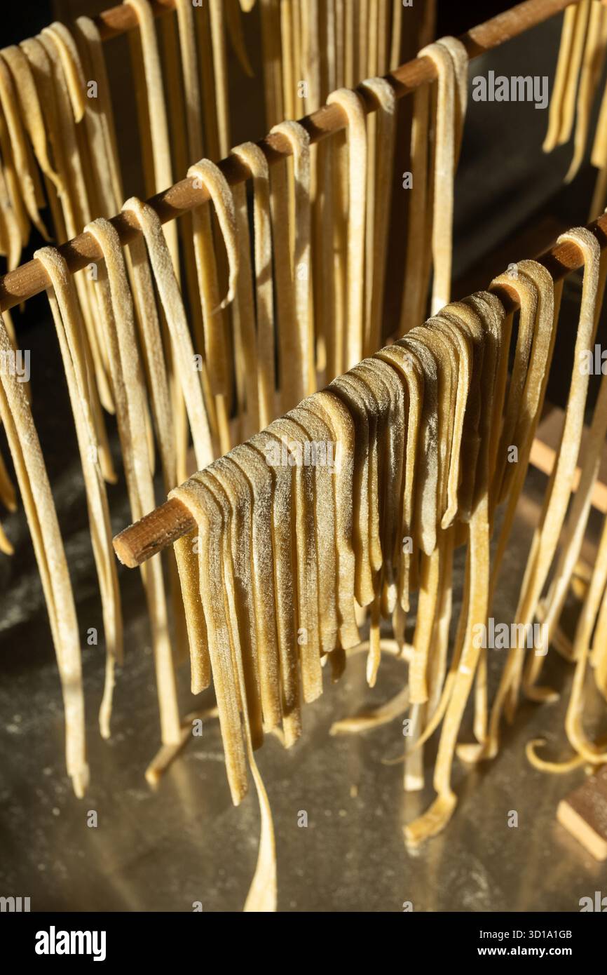 Homemade fresh Linguine pasta hanging out to dry, on a wooden frame, in close-up. Traditional home cooking and healthy eating concept. - Stock Image