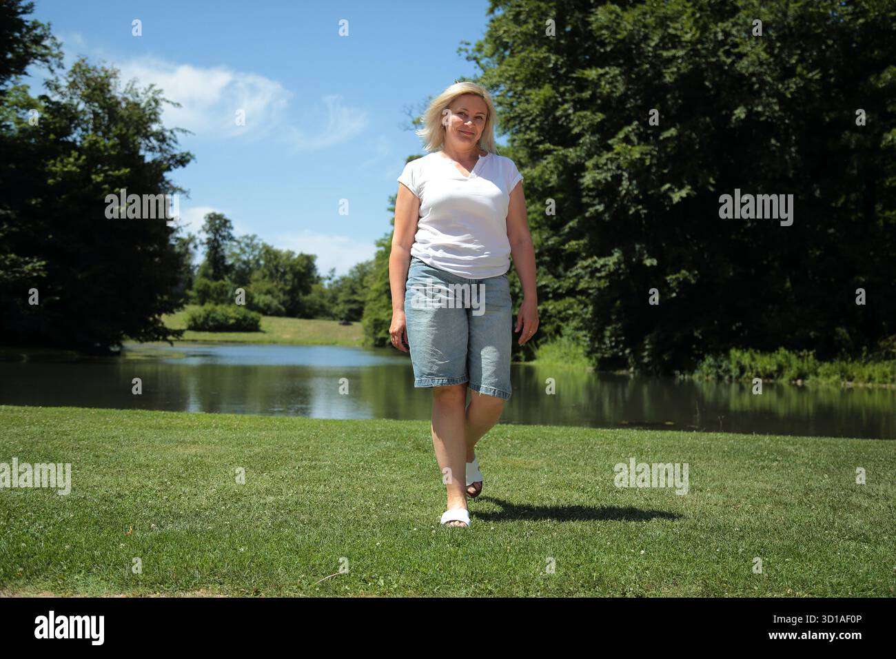 Confident Blonde Woman Walking in Nature Park Stock Photo