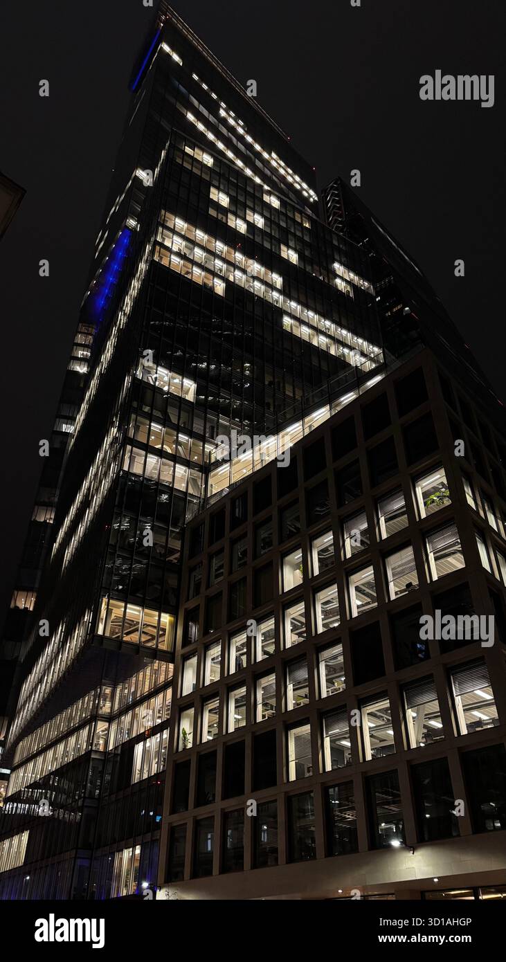 Glass and steel office tower photographed at night, with illuminated windows revealing interior floors and structure. - Smartphone Captured Stock Image