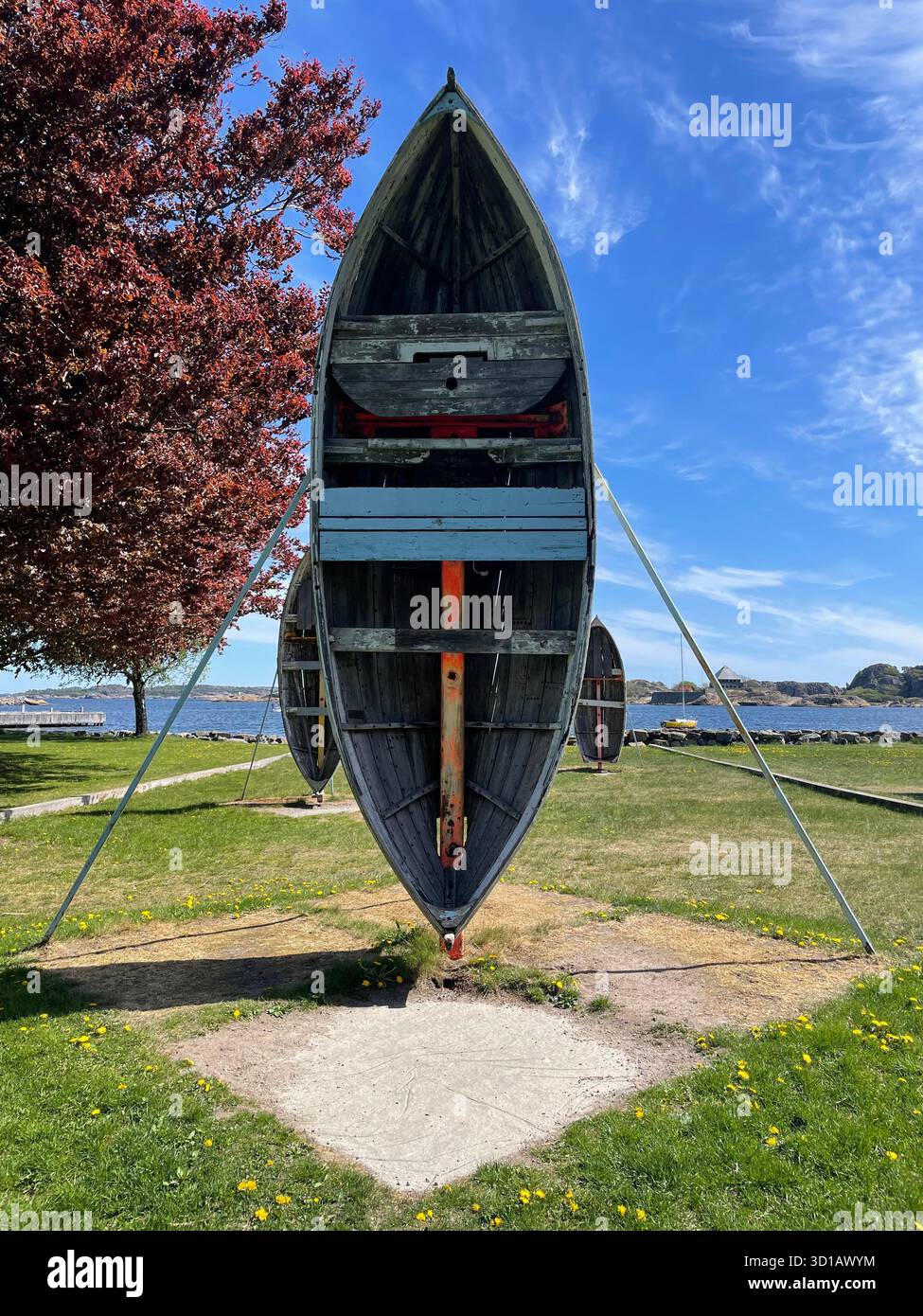 Weathered wooden boat displayed upright as an outdoor installation, symbolizing maritime heritage and the passage of time. - Smartphone Captured Stock Image