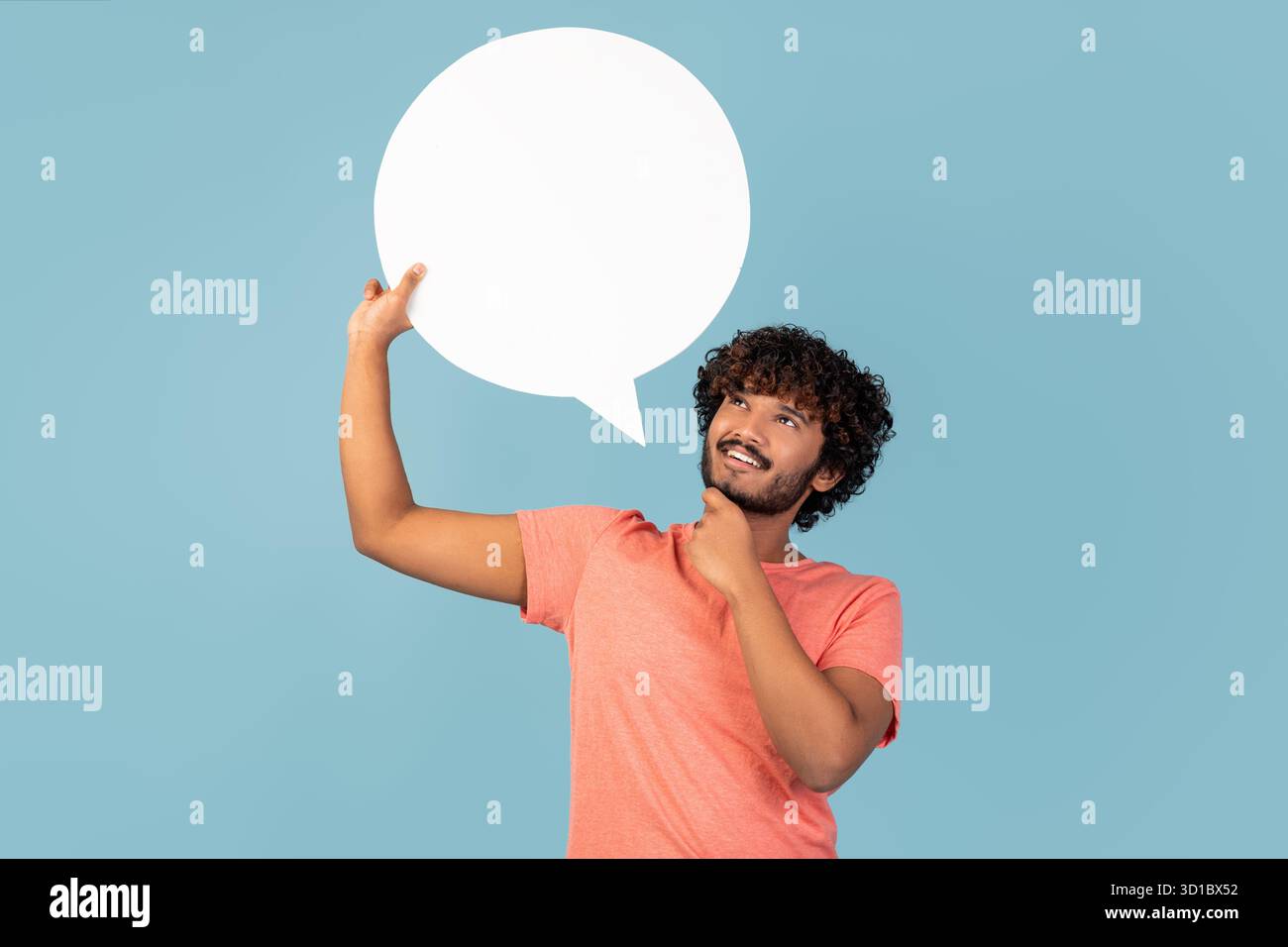 Pensive Indian Man Holding Blank Speech Bubble Considers His Thoughts in a Blue Studio Stock Photo