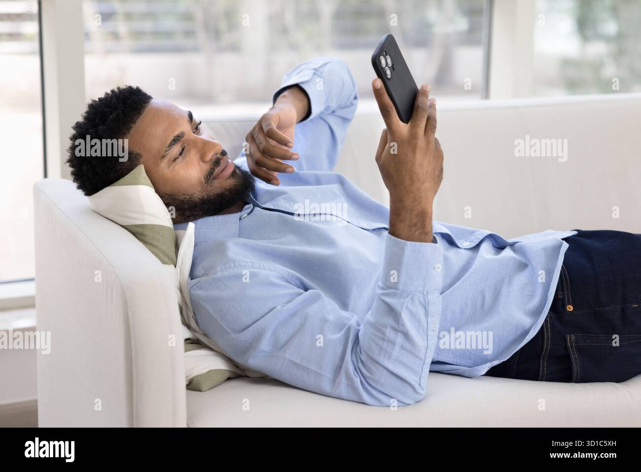 African man lying on sofa and using smartphone Stock Photo