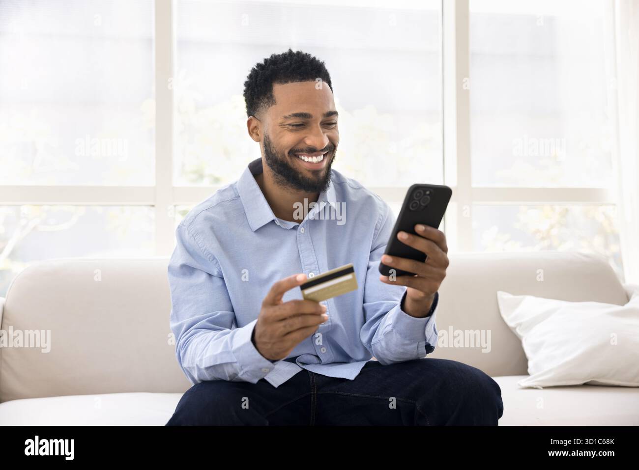 Man sit on sofa with credit card and mobile phone Stock Photo