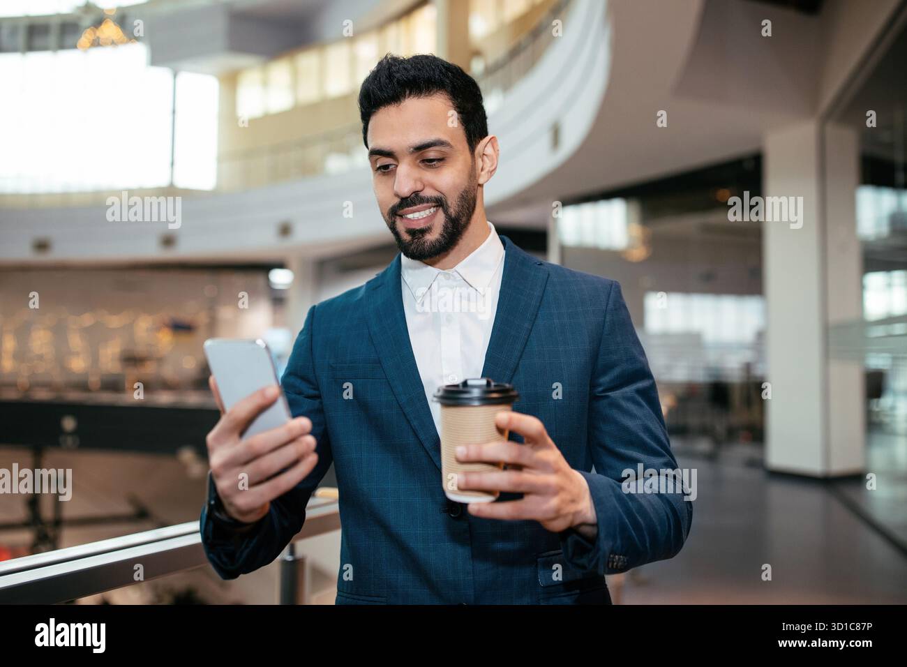 Professional Man Enjoying Coffee While Using Smartphone in Modern Office Setting Stock Photo