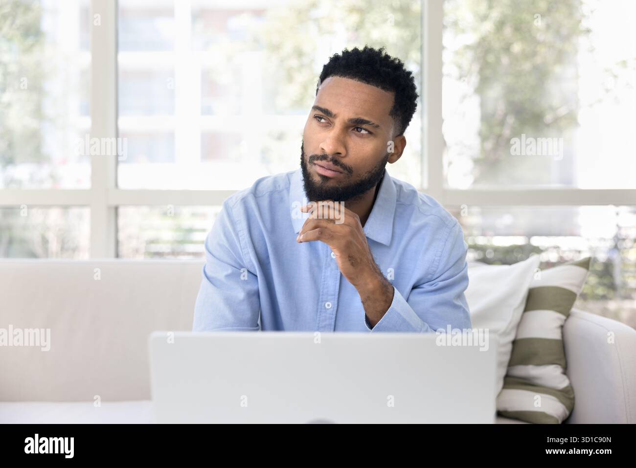 Pensive guy working on laptop looking away with thoughtful expression Stock Photo